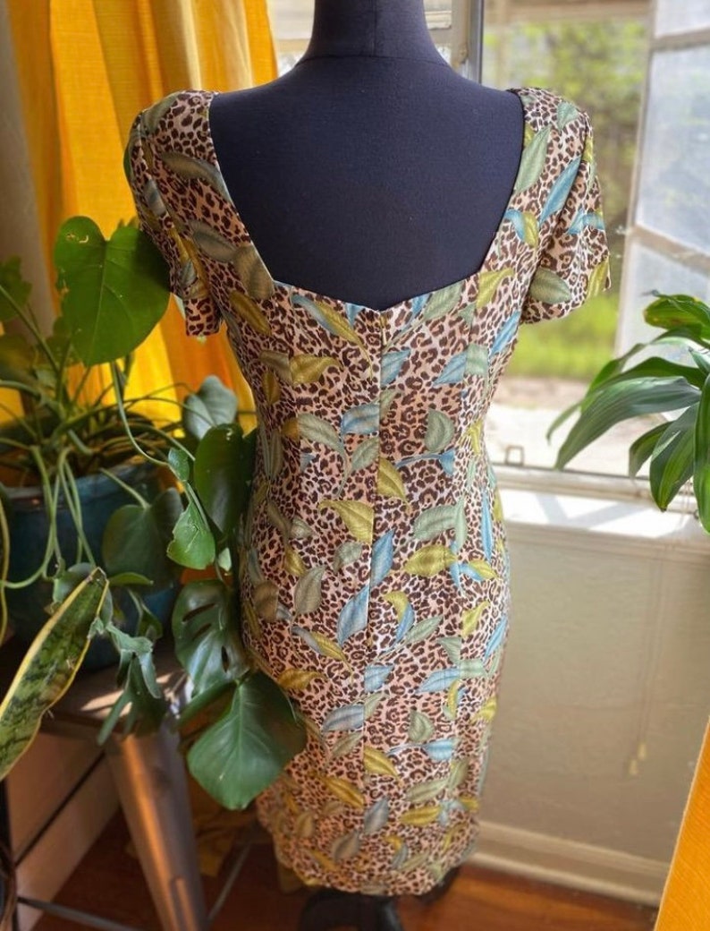 Puede incluir: Un vestido de color marr&oacute;n, verde y azul con estampado de leopardo, cuello redondo y mangas cortas. El vestido es ajustado y tiene una longitud midi.