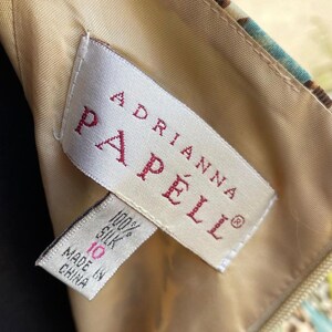 Puede incluir: Una etiqueta blanca con texto rojo que dice "Adrianna Papell" y "100% Seda" con una etiqueta de talla 10 y el texto "Hecho en China".