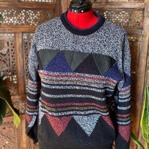 May include: A black, grey, blue, and red striped sweater with a geometric pattern. The sweater has a leather patch on the chest.
