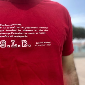 Może przedstawiać: Czerwony T-shirt z białym tekstem, który brzmi: "Benfica est éternel. Il ne connaît pas les phénomènes d'érosion qui écroulent les bâtiments les plus sûrs. Parce qu'il a toujours su ravaler sa façade. Benfica est une légende. S.L.B. Laurent Moisset 12 novembre 1991"