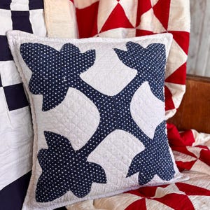 May include: A square throw pillow featuring a white quilted fabric base with a central dark blue applique pattern. The blue fabric is decorated with a small white star print. The pillow has a stitched grid texture across the white sections.