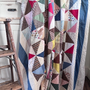 May include: A patchwork quilt featuring a variety of triangular fabric pieces in assorted colors and patterns, including floral, gingham, and heart prints. The quilt is bordered by a solid blue fabric and has a white backing.