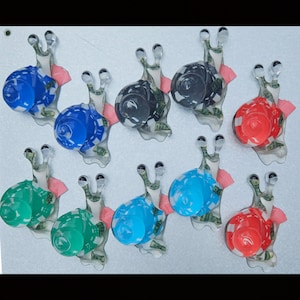 May include: A collection of ten snail-shaped figurines arranged in rows. Each snail features a translucent body with a visible green currency pattern and a solid-colored, rounded shell in shades of blue, green, red, black, and light blue.