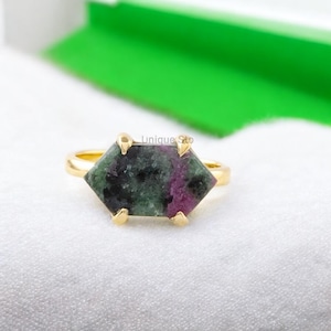 Puede incluir: Un anillo de oro con una gema hexagonal. La gema presenta una mezcla de tonos verdes y morados. El anillo tiene una banda sencilla y cuatro garras que sujetan la piedra. El texto "Unique Sto" es visible.