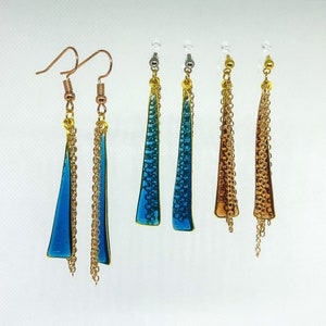 Op de afbeelding: Oorbellen in verschillende kleuren: blauw, turquoise en brons. Elke oorbel heeft een driehoekige hanger met een textuurontwerp en een gouden ketting. Gepresenteerd op een witte achtergrond.