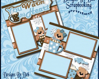 Op de afbeelding: Een printbaar scrapbookpapierontwerp met een blauw en bruin kleurenschema met een winterthema. Het ontwerp bevat beren, sneeuwvlokken en de tekst "You Warm My Heart".
