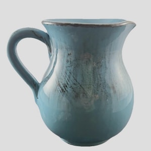 May include: A ceramic pitcher with a rounded body and a curved handle. The pitcher is glazed in shades of blue with darker accents and a dark rim. The design is simple and elegant, suitable for serving beverages or as a decorative piece.