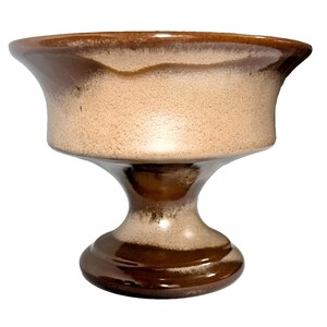 May include: A ceramic pedestal bowl featuring a wide, flared rim and a sturdy, rounded base. The surface displays a two-tone glaze with a speckled, light beige center that transitions into a smooth, glossy dark brown at the rim and base.