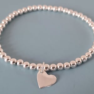 Op de afbeelding: Een zilveren armband met kralen en een klein zilveren hartje.