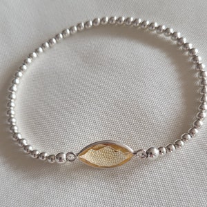 Puede incluir: Un brazalete de cuentas de plata con un solo dije de piedra preciosa amarilla.