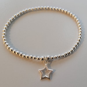 Könnte beinhalten: Ein silbernes Armband mit Perlen und einem Sternanhänger. Das Armband besteht aus kleinen, runden Perlen und hat ein schlichtes, elegantes Design.