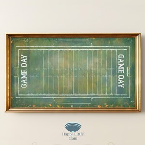 Op de afbeelding: Een rechthoekig ingelijst wandkunstwerk met een afbeelding van een groen American footballveld met witte lijnen en de tekst GAME DAY verticaal gedrukt aan zowel de linker- als rechterkant. Het kunstwerk zit in een goudkleurige metalen lijst.