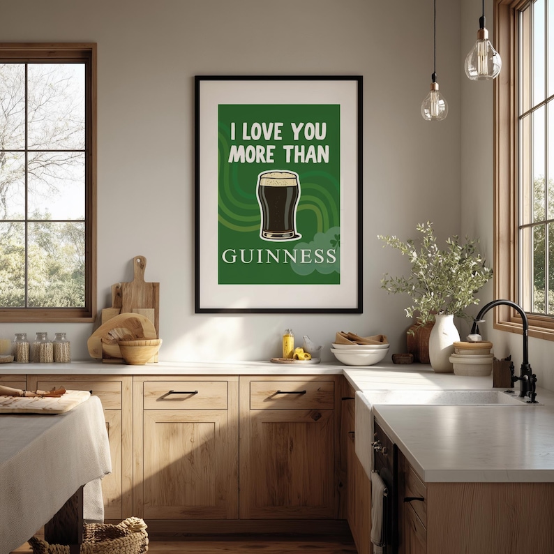 May include: A framed print featuring a pint of Guinness on a green background, with the text "I LOVE YOU MORE THAN" above and "GUINNESS" below. The print is in a black frame and is displayed in a kitchen setting.