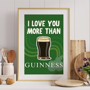 May include: A framed print featuring the words "I love you more than Guinness" above a pint of stout. The background is green with curved lines. The print is in a gold frame, suitable for a kitchen or bar.