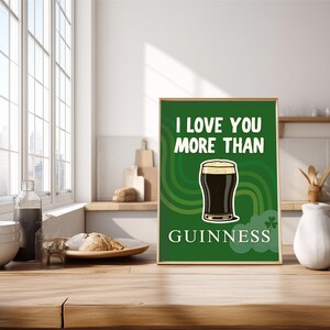 May include: A framed green print with the text "I LOVE YOU MORE THAN GUINNESS" and a graphic of a pint of Guinness. The print is displayed on a wooden surface in a kitchen setting.