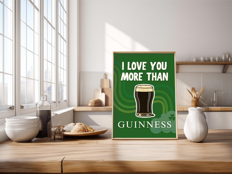 May include: A framed green print with the text "I LOVE YOU MORE THAN GUINNESS" and a graphic of a pint of Guinness. The print is displayed on a wooden surface in a kitchen setting.