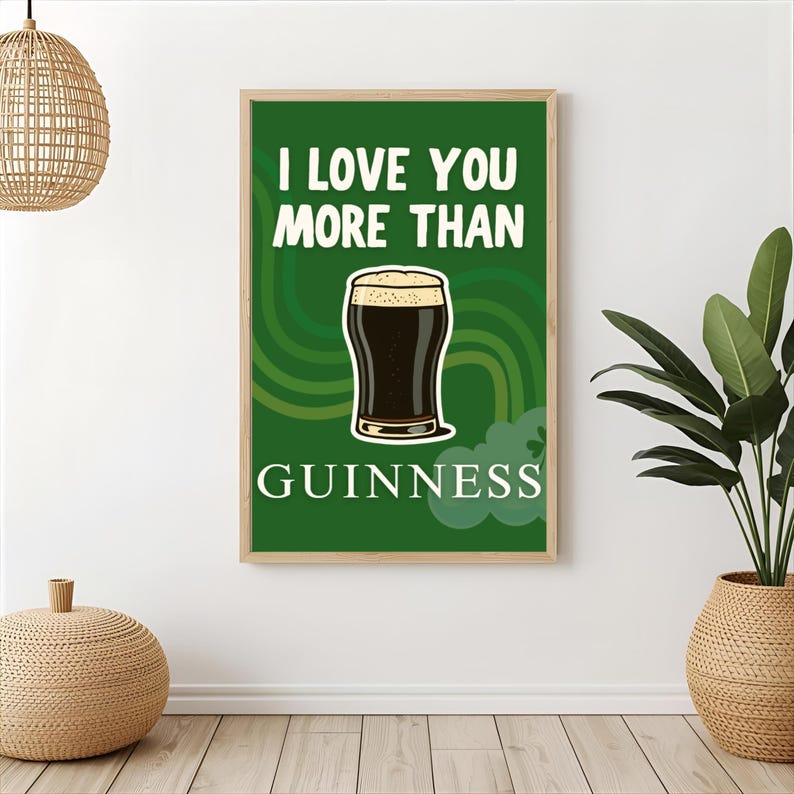 May include: A framed green poster with the text "I LOVE YOU MORE THAN GUINNESS" and an illustration of a pint of Guinness. The poster is in a wooden frame and is on a white wall.