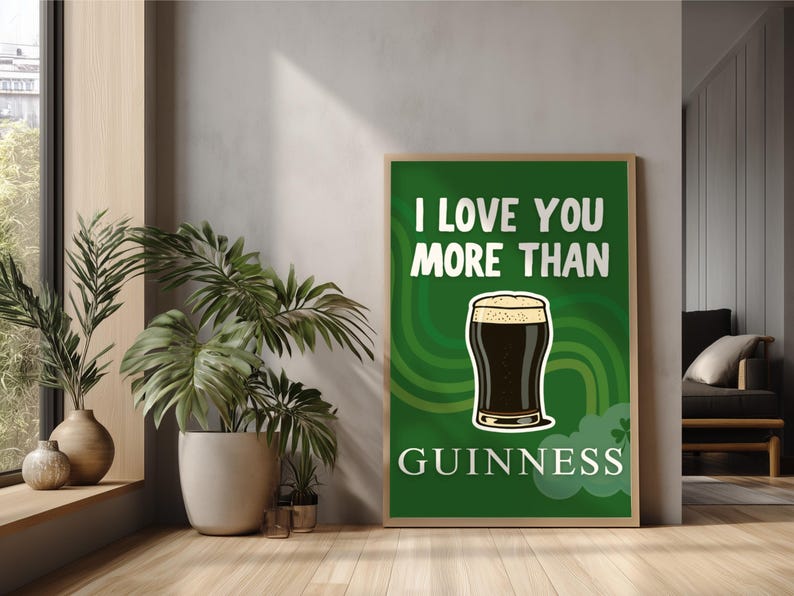 May include: A framed poster with the text "I LOVE YOU MORE THAN GUINNESS" on a green background. The poster features a cartoon pint of Guinness. The poster is in a room with plants and a window.