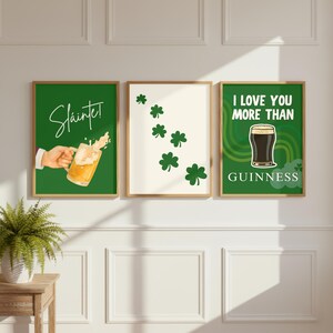 May include: Three framed art prints with a St. Patrick's Day theme. One print features a hand holding a beer mug with the word "Sl&aacute;inte!". Another has green shamrocks on a cream background. The third print says "I LOVE YOU MORE THAN GUINNESS".