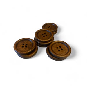 May include: A set of six brown wooden buttons, each with four holes. The buttons are arranged in a triangular shape.
