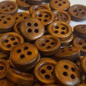 May include: A collection of brown wooden buttons, each with four holes. The buttons are arranged in a random pattern and are all the same size.