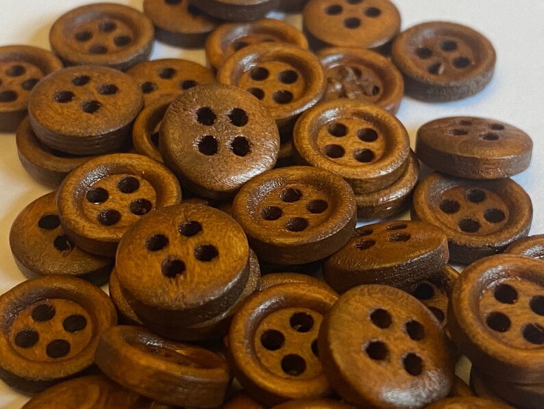 May include: A collection of brown wooden buttons, each with four holes. The buttons are arranged in a random pattern and are all the same size.