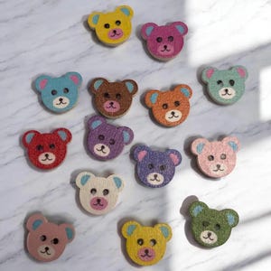May include: A selection of wooden bear-shaped buttons in a variety of colours, such as yellow, pink, blue, brown, orange, green, purple, and white. Each button has a painted face and ears, and measures approximately 2.5 cm in diameter.