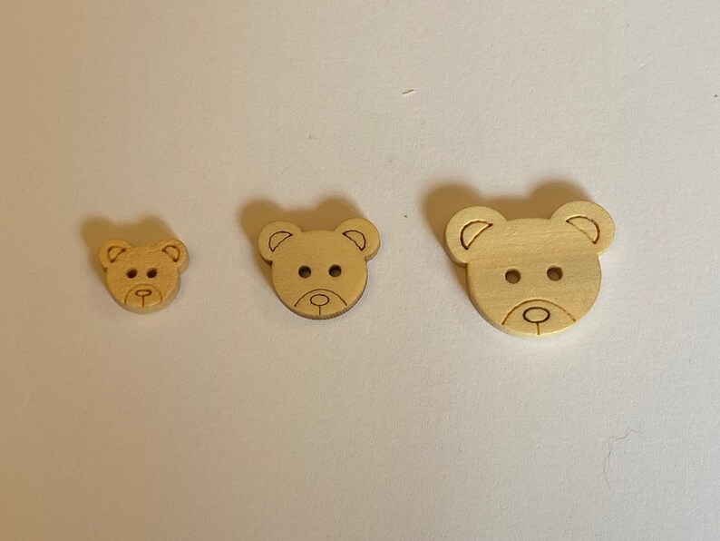 Pode incluir: Tr&ecirc;s bot&otilde;es de madeira em forma de urso em tamanhos diferentes. Os bot&otilde;es s&atilde;o de cor castanho claro e t&ecirc;m um design simples.