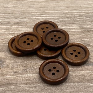 May include: A group of eight brown wooden buttons with four holes each. The buttons are arranged in a circle on a wooden surface.