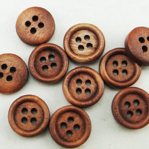 May include: A collection of ten brown wooden buttons, each with four holes. The buttons are arranged in a random pattern on a white surface.