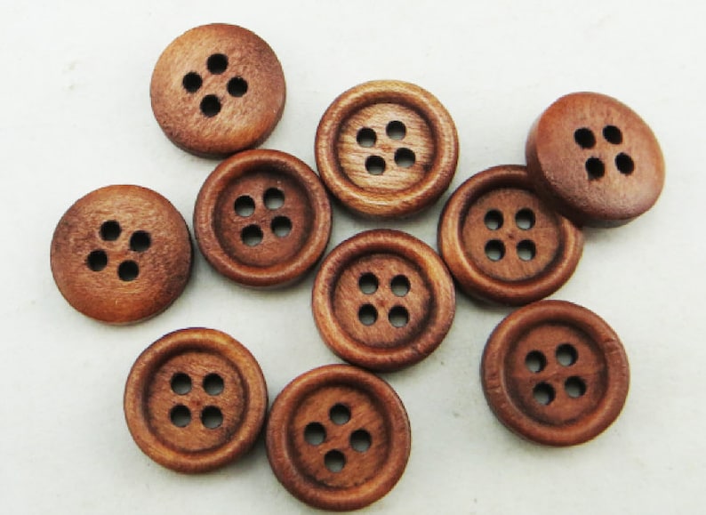 May include: A collection of ten brown wooden buttons, each with four holes. The buttons are arranged in a random pattern on a white surface.