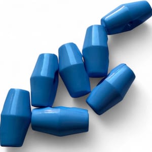 May include: Seven blue plastic beads are scattered across a white surface. Each bead has a distinctive geometric shape. The beads are a vibrant shade of blue and have a smooth, glossy finish.