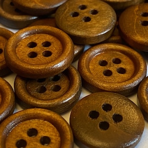 May include: A close-up of a group of brown wooden buttons, each with four holes. The buttons are arranged in a random pattern and are all the same size.