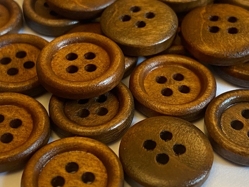 May include: A close-up of a group of brown wooden buttons, each with four holes. The buttons are arranged in a random pattern and are all the same size.