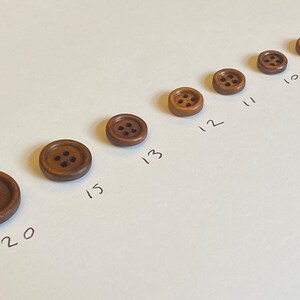 May include: A set of nine brown wooden buttons with four holes each, arranged in a line from smallest to largest. The buttons are labelled with numbers 9 through 20.