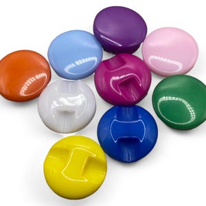 May include: Assortment of colourful plastic buttons with a variety of shapes and sizes. Some buttons have a raised design.
