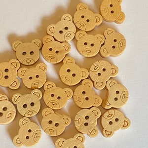 Pode incluir: Uma cole&ccedil;&atilde;o de bot&otilde;es de madeira em forma de urso em uma cor marrom claro. Os bot&otilde;es t&ecirc;m um design simples com dois olhos, um nariz e uma boca.