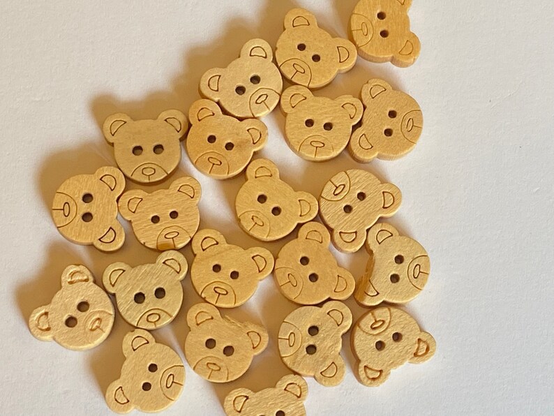 Pode incluir: Uma cole&ccedil;&atilde;o de bot&otilde;es de madeira em forma de urso em uma cor marrom claro. Os bot&otilde;es t&ecirc;m um design simples com dois olhos, um nariz e uma boca.