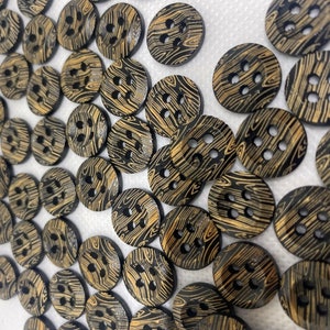 May include: A large group of black and gold wooden buttons with a wood grain pattern. The buttons have four holes each.