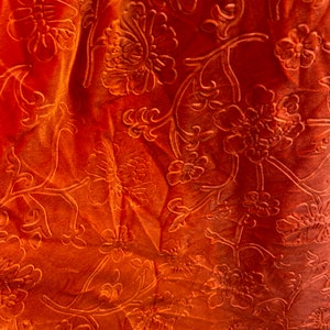 May include: Orange fabric with an embossed floral pattern. The fabric has a soft, velvety texture.