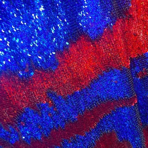 May include: A close-up of a fabric with blue and red sequins arranged in a zig-zag pattern. The sequins are iridescent and reflect light.