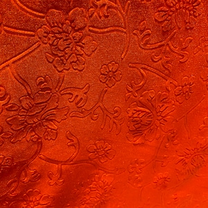 May include: Orange fabric with an embossed floral pattern. The fabric has a textured, velvety feel.