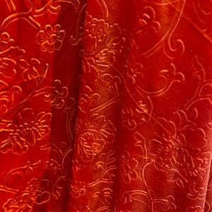 May include: Close-up of a rust-colored fabric with an embossed floral pattern. The fabric has a soft, velvety texture.
