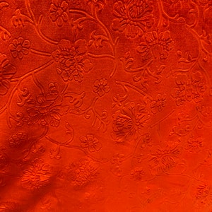 May include: Orange fabric with an embossed floral pattern. The fabric has a raised texture and a rich, vibrant color.
