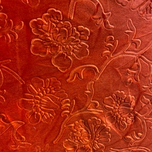 May include: Close-up of a rust-colored fabric with an embossed floral pattern. The fabric has a soft, velvety texture.