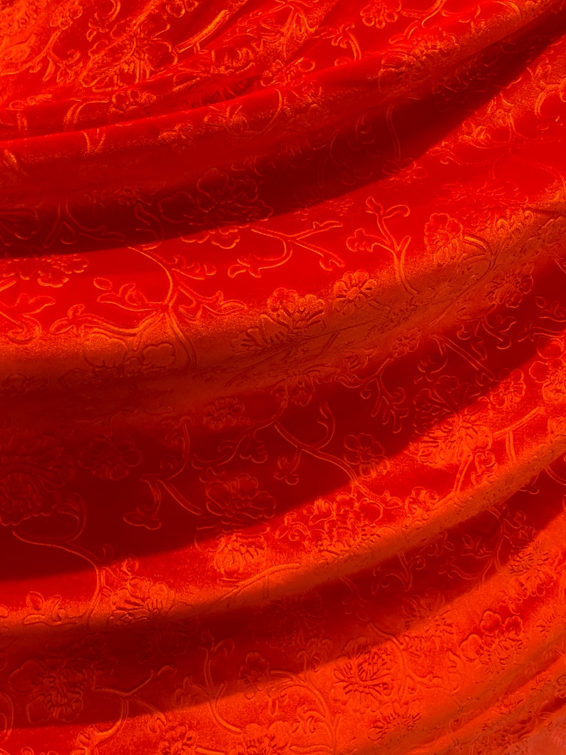 May include: Orange fabric with a floral pattern. The fabric is soft and velvety.