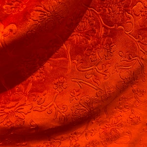 May include: Orange fabric with an embossed floral pattern. The fabric has a soft, velvety texture.