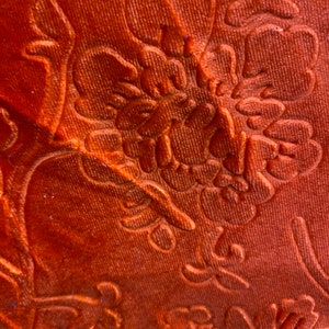 May include: Close-up of a textured orange fabric with a floral pattern. The fabric has a slightly shiny finish.