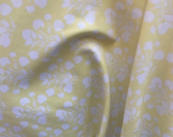 May include: A yellow fabric with a white floral pattern. The fabric is wrinkled and has a soft, silky texture.