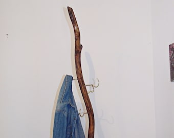 May include: A wooden coat rack made from a natural branch with four metal hooks. A blue denim jacket is hanging on one of the hooks.